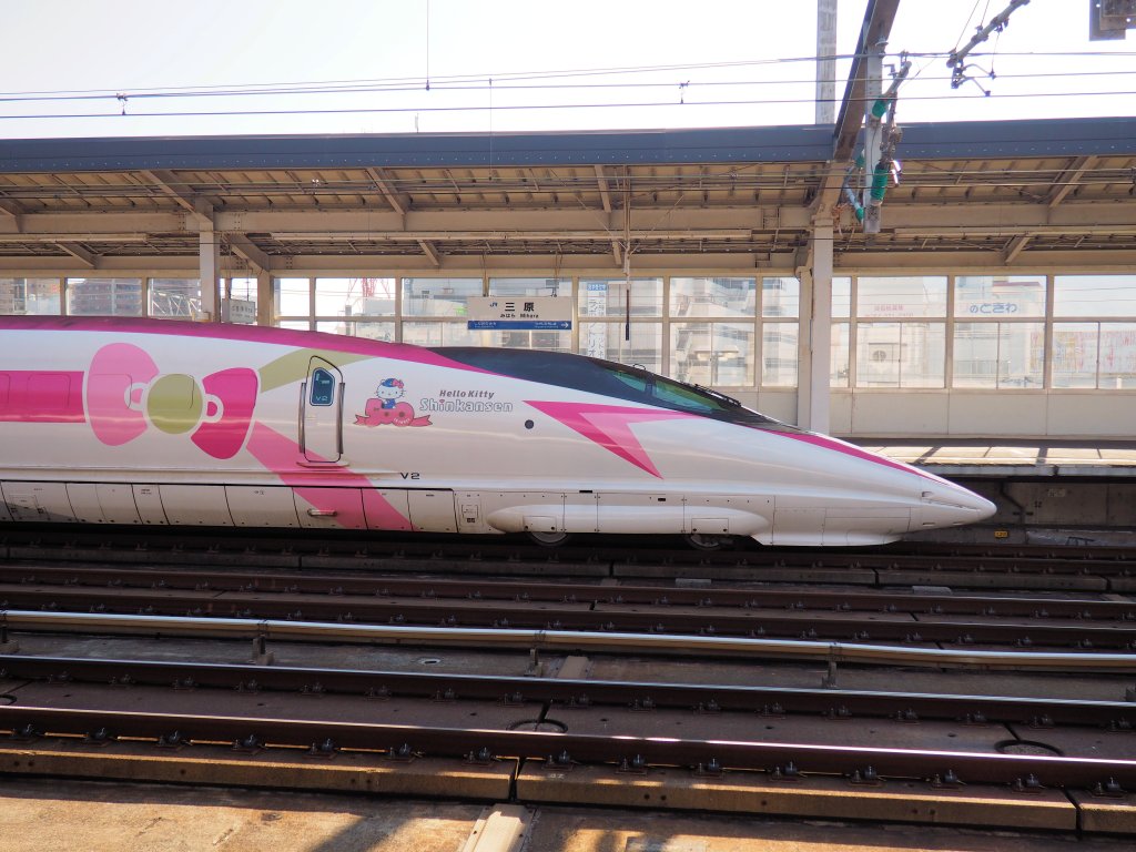 A shinkansen high-speed train fills the image. There is a lot of pink colouration on the train and a large bow motif covers some of the train. There is a small image of Hello Kitty with the words 'Hello Kitty Shinkansen' next to it.